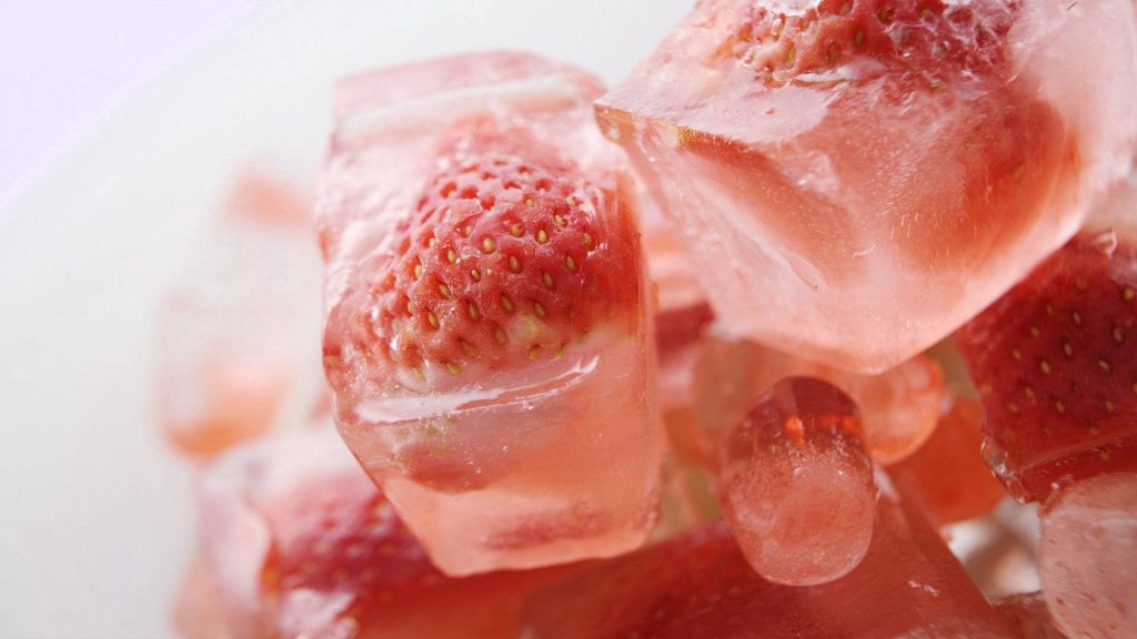 High-resolution macro wallpaper of vibrant strawberries frozen in clear ice cubes with bright lighting