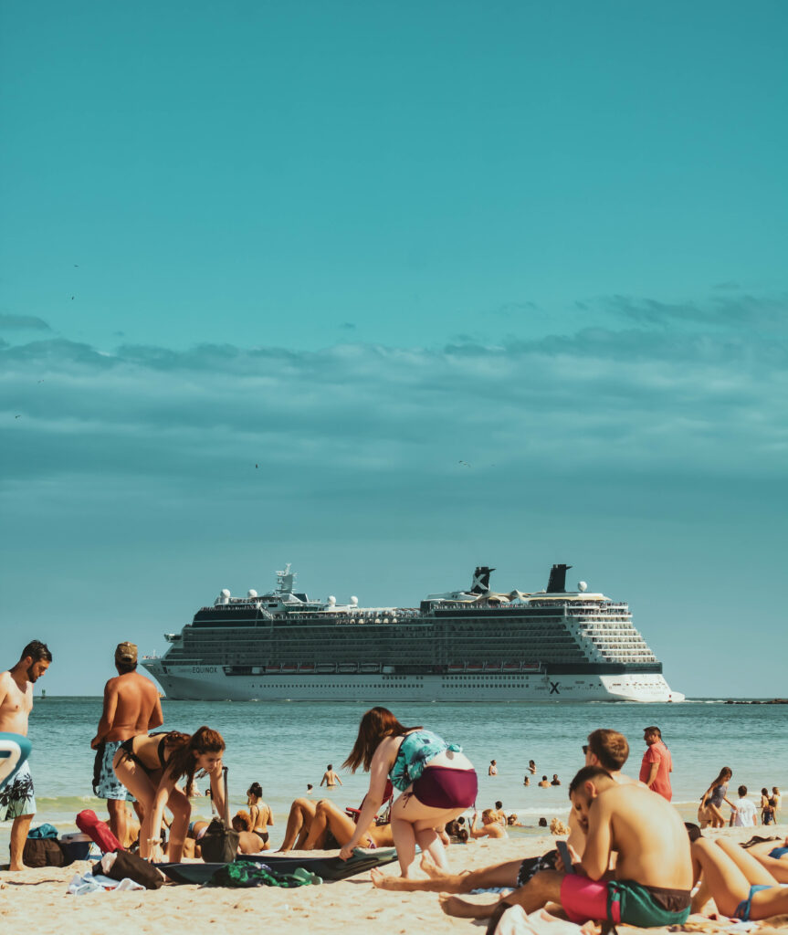 Vibrant beach with sunbathers swimmers and cruise ship under clear sky summer vacation scene Wallpaper