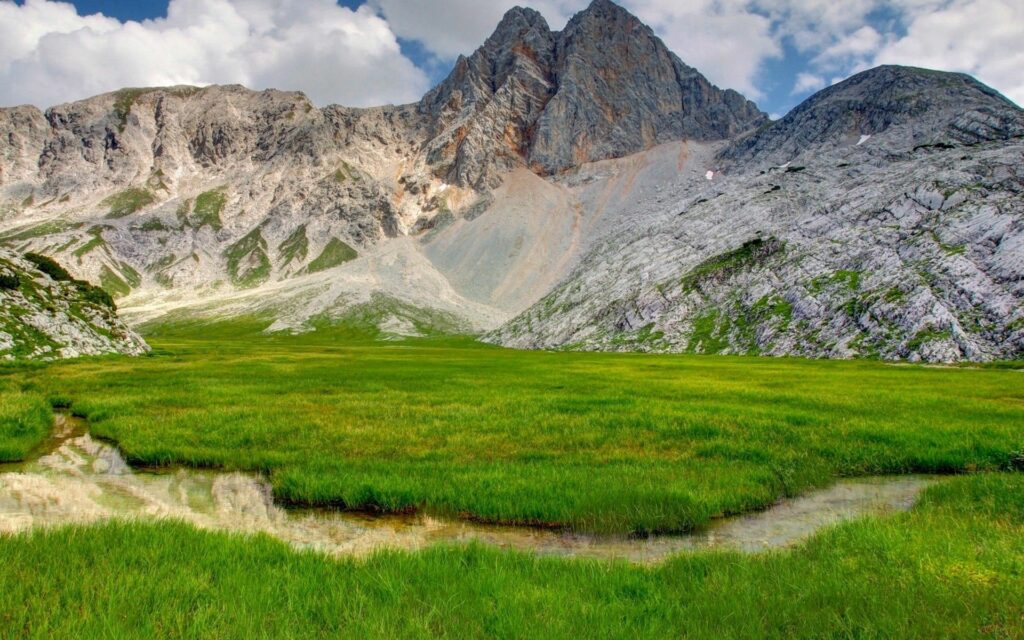 Vibrant summer landscape with lush grass rugged rocks towering mountains bright sky wallpaper