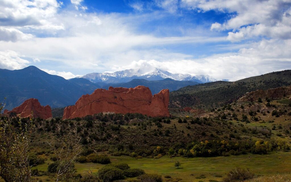 Scenic summer landscape with green grass red rock formations snow-capped mountains clear sky Wallpaper