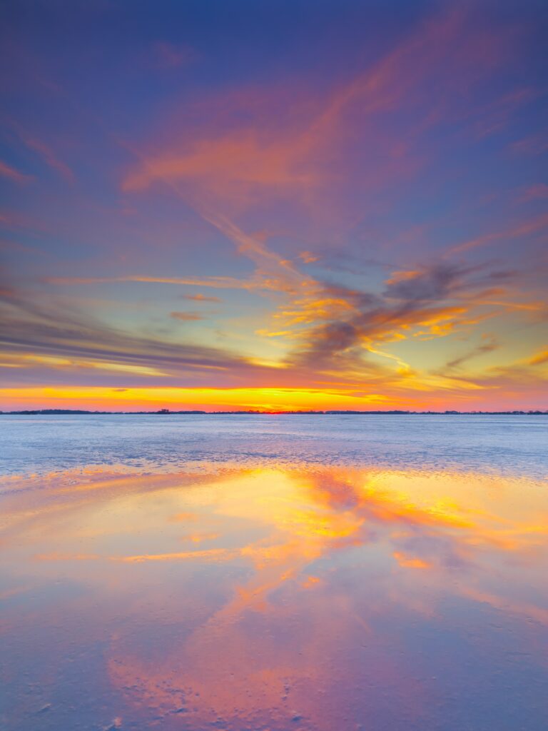 Vibrant sunset horizon over calm sea with orange pink and purple sky reflected on water surface Wallpaper