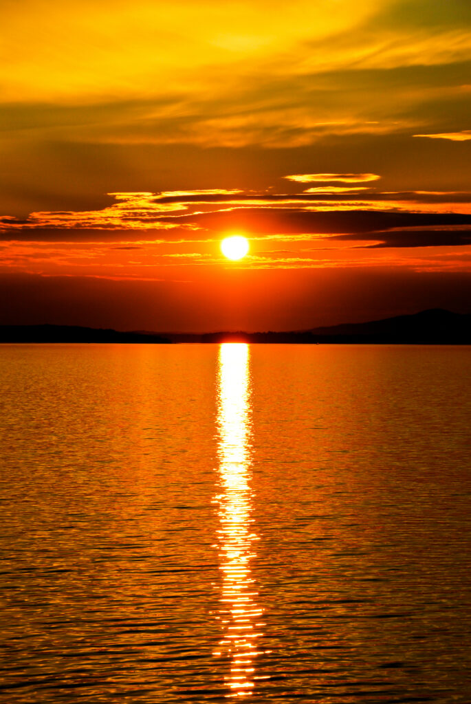 Vibrant sunset over calm waters with glowing sun orange gold hues dramatic clouds lens flare Wallpaper