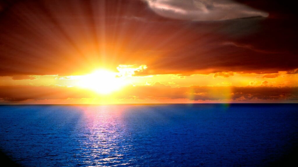 Vibrant sunset with sunbeams over rippling sea and colorful sky horizon wallpaper background