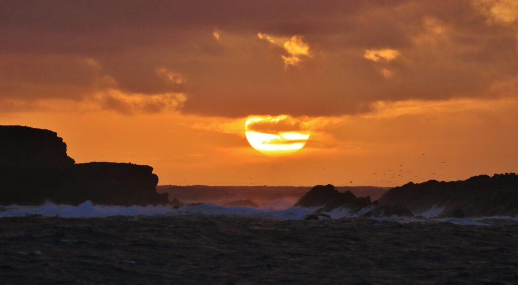 Vibrant sunset over rugged coastal cliffs with orange gold skies and dramatic sea landscape wallpaper