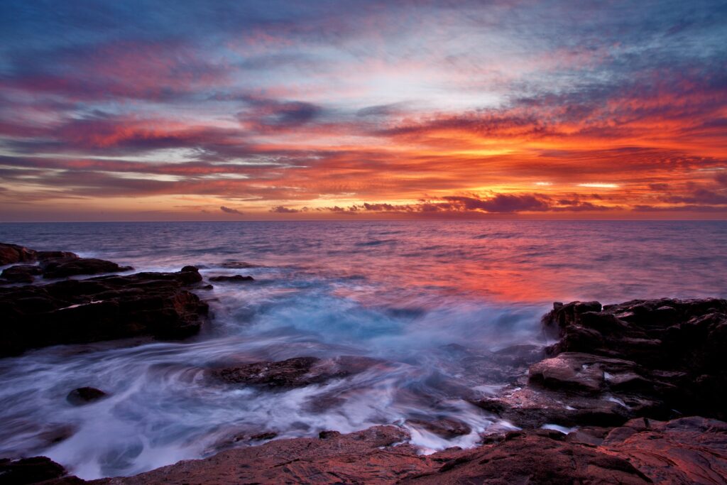 Vibrant sunset seascape with dramatic clouds soft waves and rugged coastal rocks wallpaper