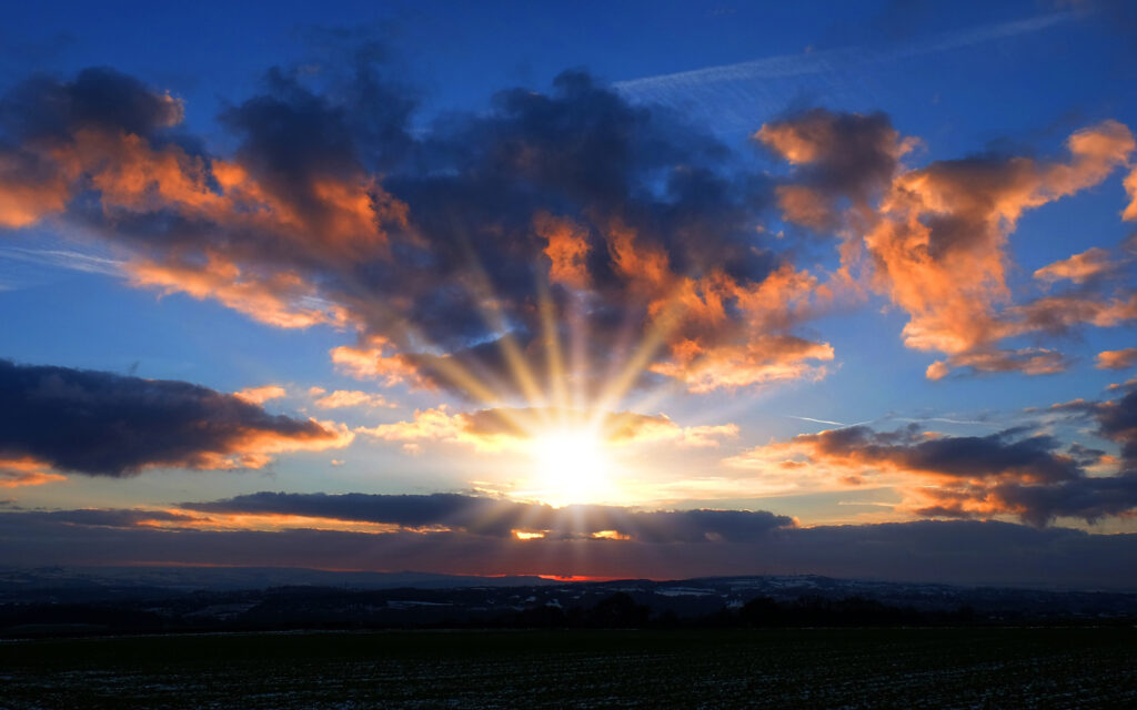 Vibrant sunset sky with golden sunlight bursting through dramatic clouds over horizon wallpaper