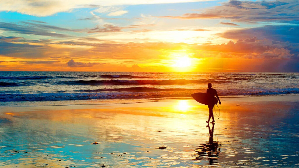 Surfer Silhouette Against Vibrant Sunset Beach Background Wallpaper