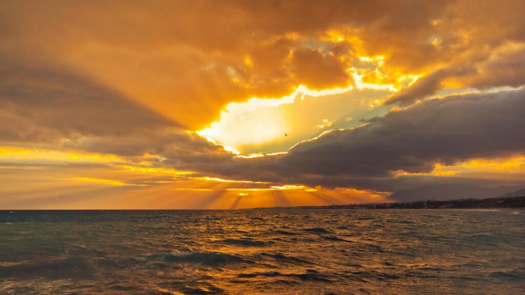 Vibrant sunset wallpaper with golden sunlight breaking through clouds over ocean waves
