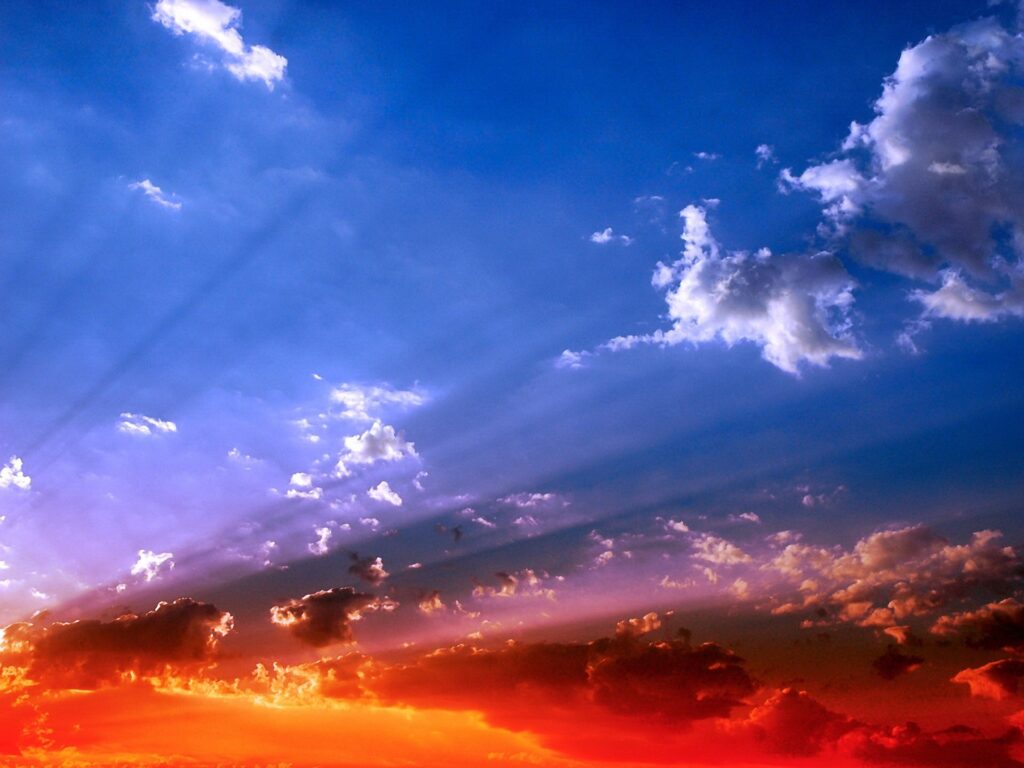 Sunset wallpaper with vibrant orange and deep blue sky and sunlight beams through clouds