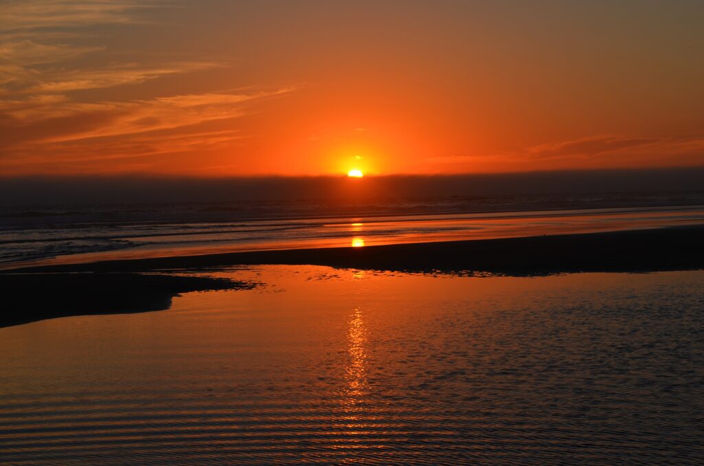 Vibrant sunset wallpaper with glowing sun setting over calm sea and warm orange gold reflections