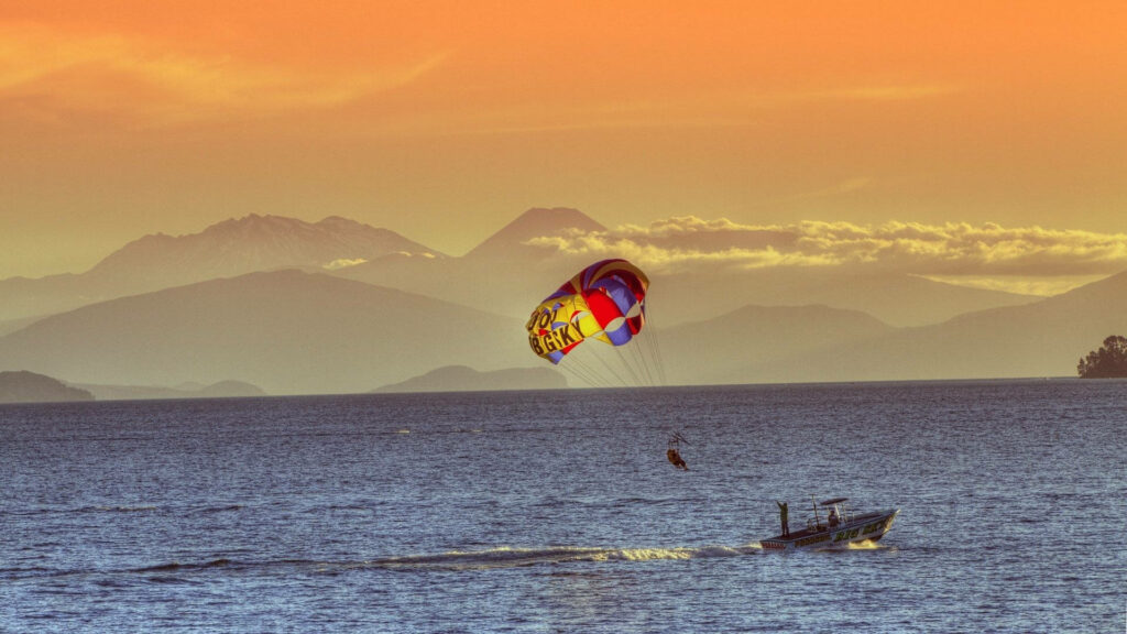 Vibrant Sunset with Boat, Parasailor Launch & Dramatic Mountains Wallpaper