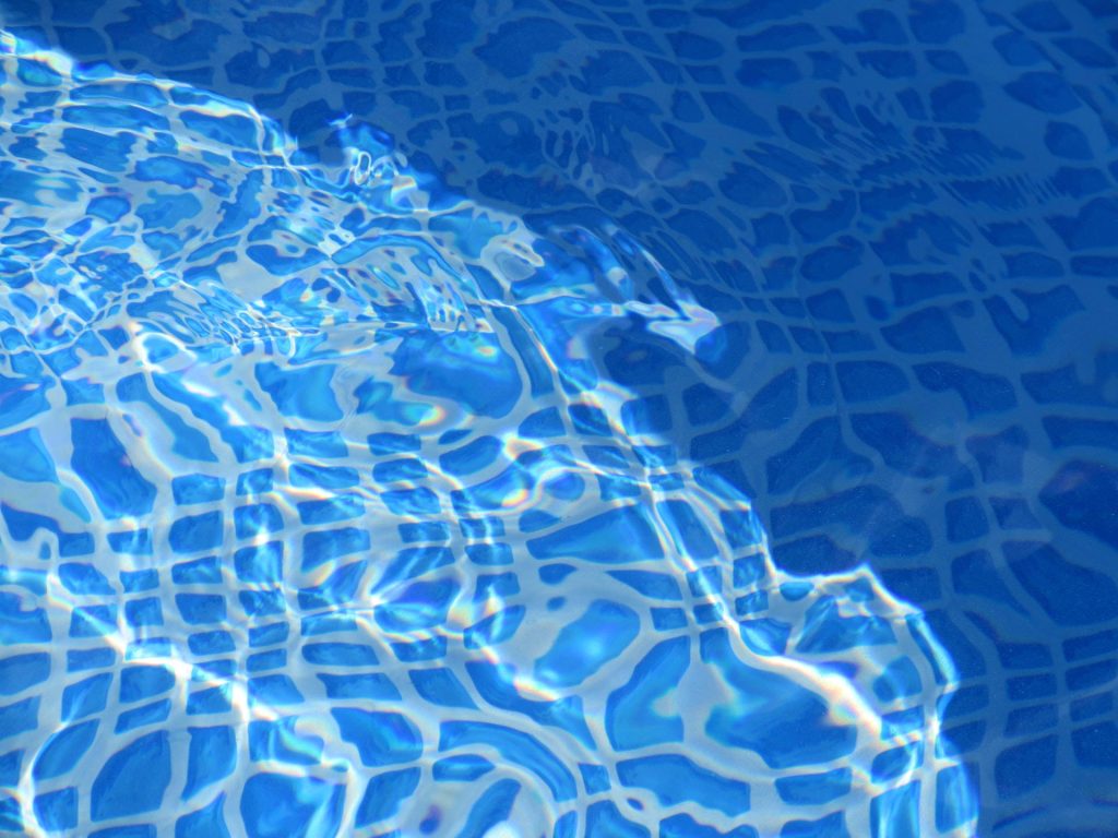 Vibrant swimming pool wallpaper with sunlight reflecting on blue mosaic tiles and rippling water
