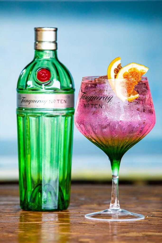 Tanqueray No Ten Gin bottle with pink citrus cocktail on rustic table vibrant wallpaper background