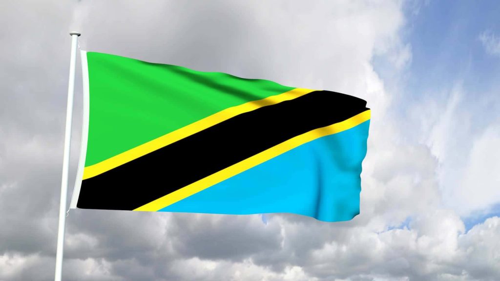Tanzania national flag waving on white pole with vibrant colors against soft cloudy sky background Wallpaper