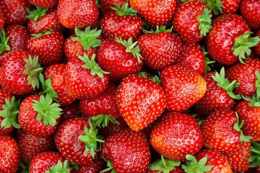Top-angle close-up of fresh ripe strawberries with green leaves juicy vibrant fruit background Wallpaper
