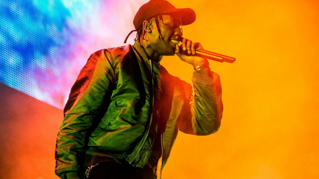 Travis Scott live concert in bomber jacket vibrant orange yellow stage lights blue background wallpaper