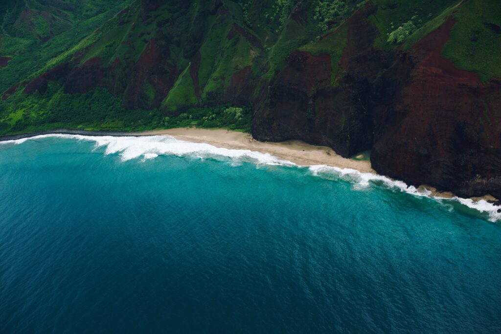 Aerial view of vibrant coastline with turquoise waves golden sands rugged rocks and mossy cliffs Wallpaper