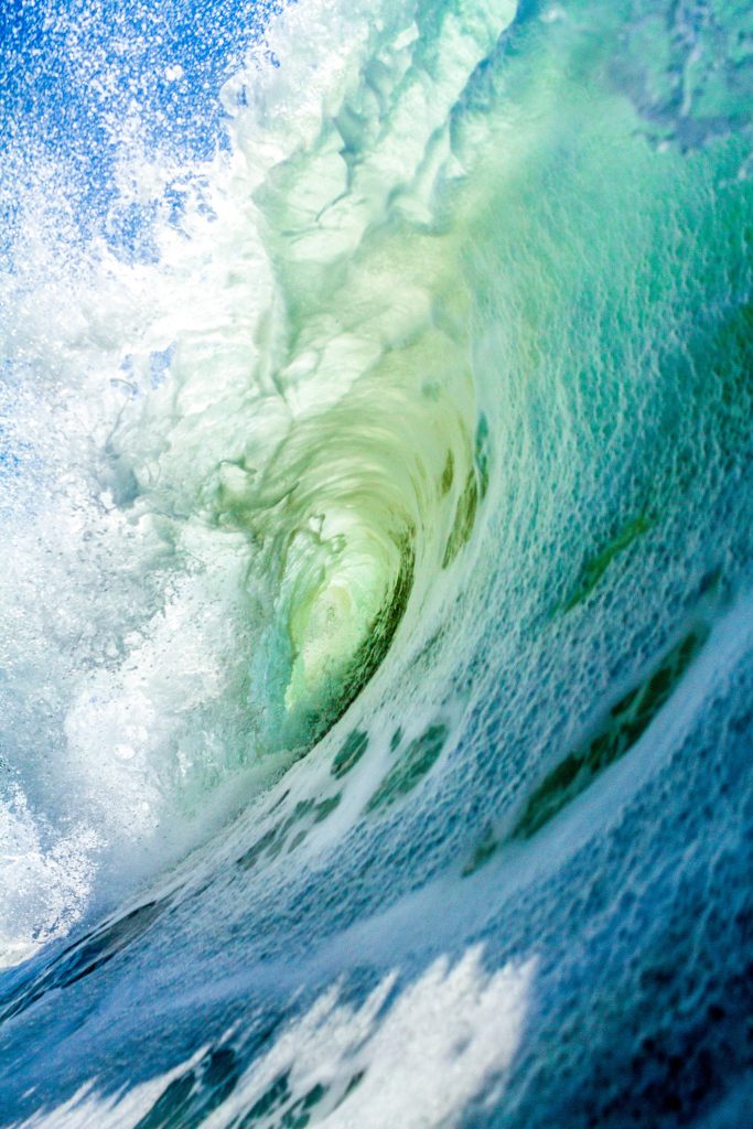 Close-up vibrant turquoise ocean wave breaking with sunlight glowing through foaming water barrel Wallpaper