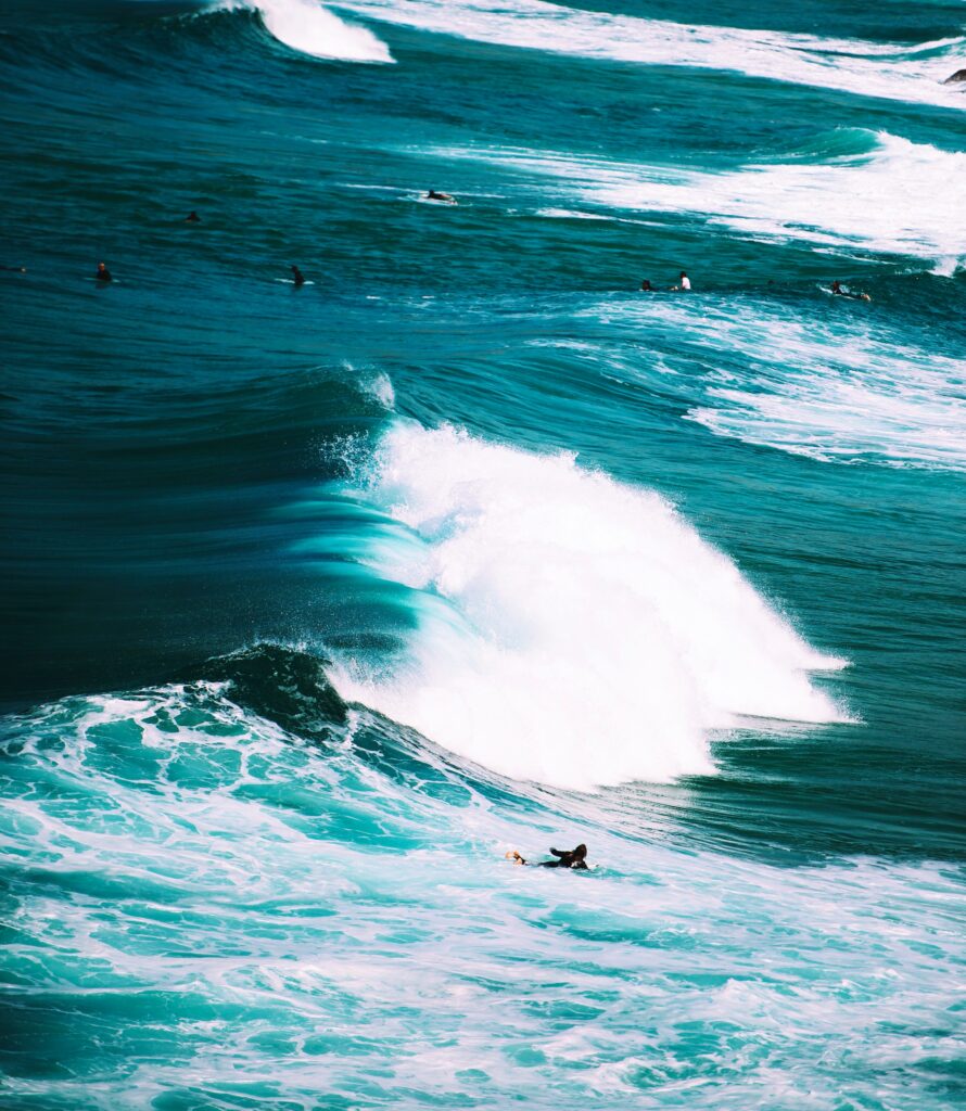Turquoise ocean waves with white surf and surfers riding under bright daylight high resolution wallpaper