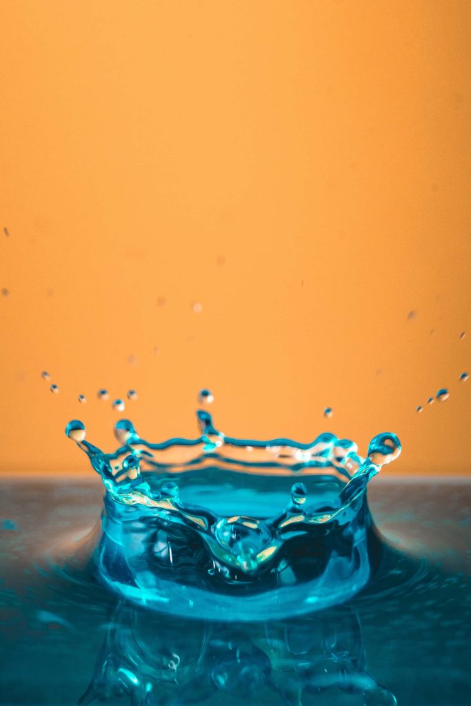 High-speed macro photo of a turquoise water splash crown on warm amber background abstract wallpaper