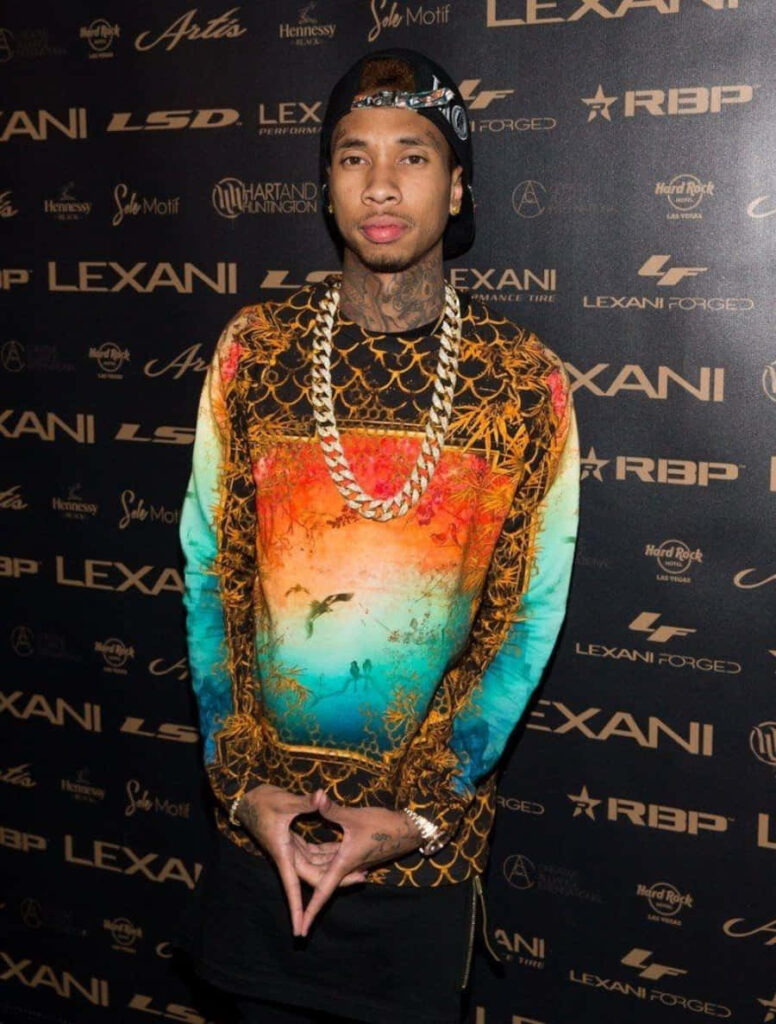 Colorful Tyga Wallpaper: Confident Rapper in Vibrant Chains & Logos