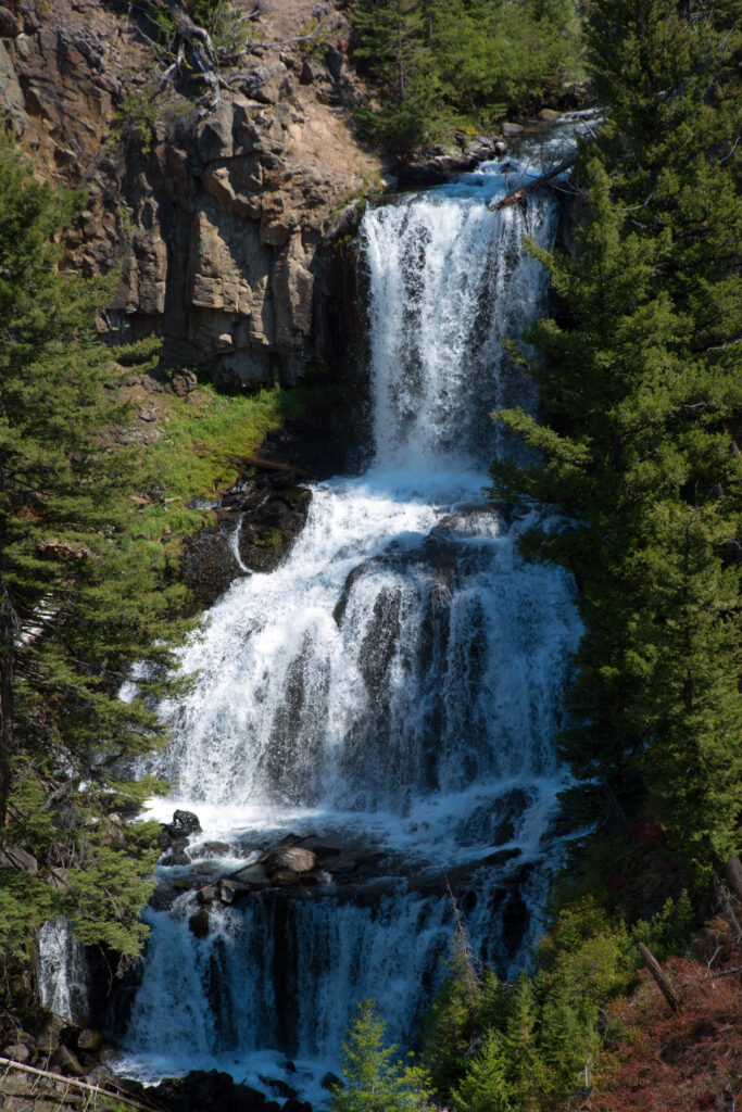 Vibrant waterfall cascading over rugged rocks with lush green forest and clear flowing river Wallpaper