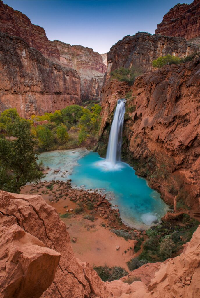 Vibrant waterfall flowing over red cliffs into turquoise pool with lush greenery and rocks wallpaper