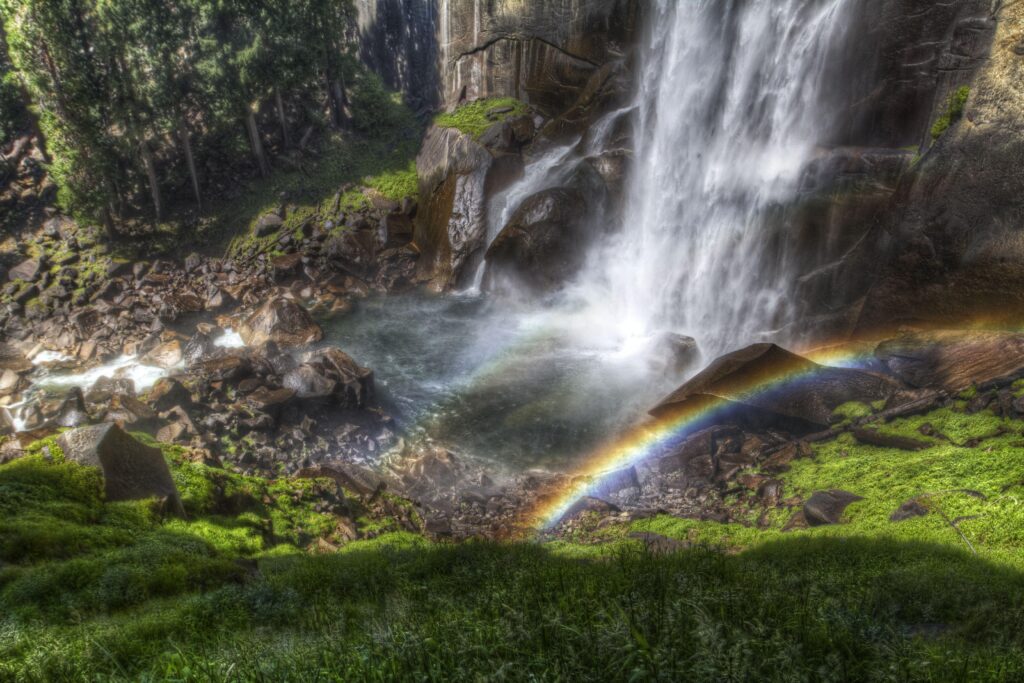 Vibrant waterfall cascading over stones with colorful rainbows lush greenery and misty stream wallpaper