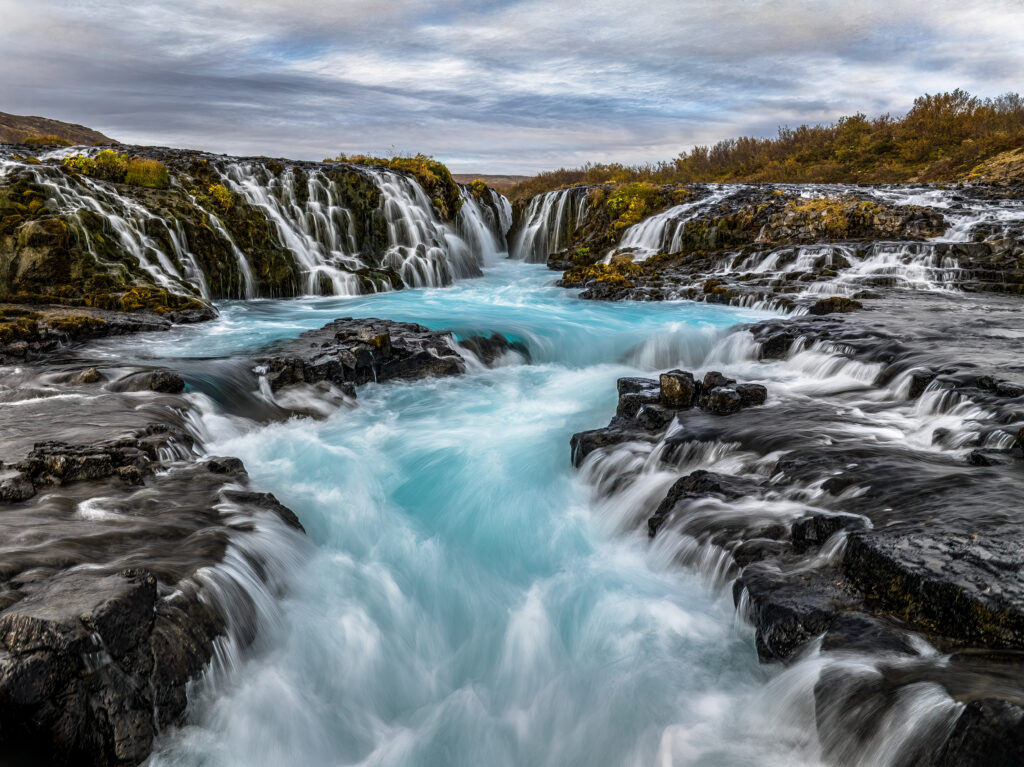 Vibrant waterfall cascading over rugged rocks with lush greenery and vivid blue water background Wallpaper