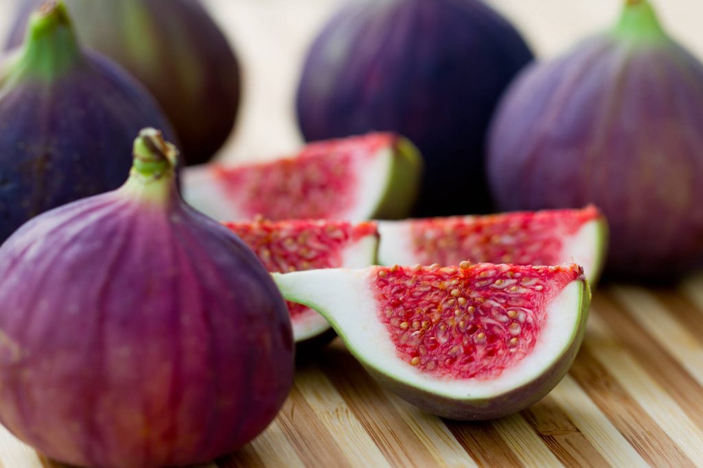 Macro photo of fresh ripe wedged purple figs with juicy red interiors on wooden surface Wallpaper