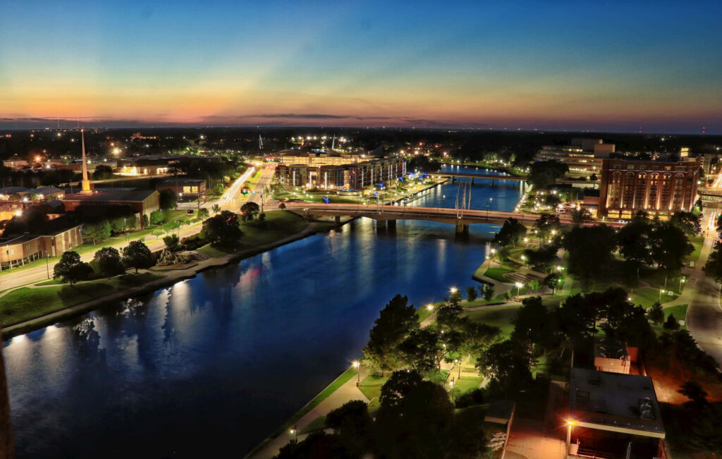 Vibrant Wichita Night Scene: City Lights Reflecting on Calm Waters Wallpaper