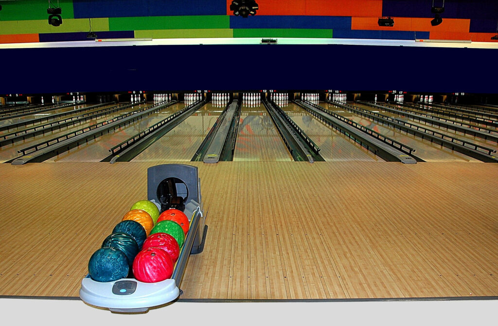 Wide bowling alley with polished lanes colorful balls and bold geometric ceiling patterns wallpaper