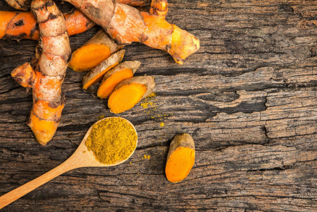 Vibrant Wooden Background with Fresh Turmeric Roots and Powder Wallpaper