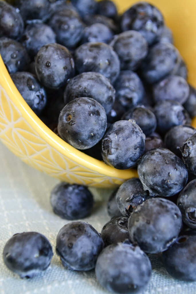 Yellow bowl overflowing with ripe deep blue huckleberries on soft fabric background wallpaper