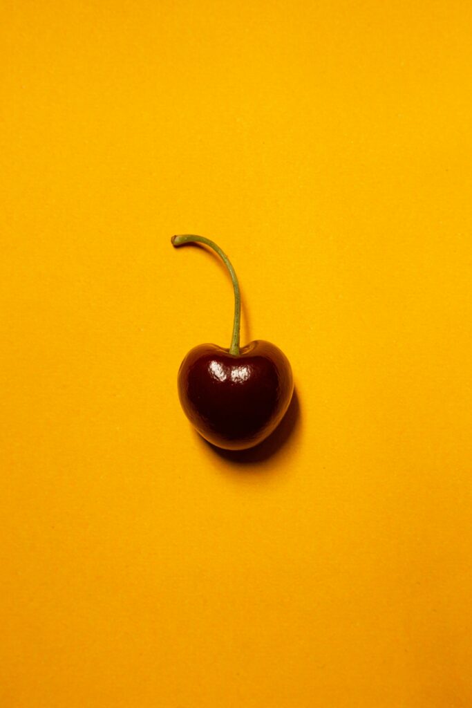 Vibrant Yellow Background with a Single Red Cherry - Minimalist Wallpaper