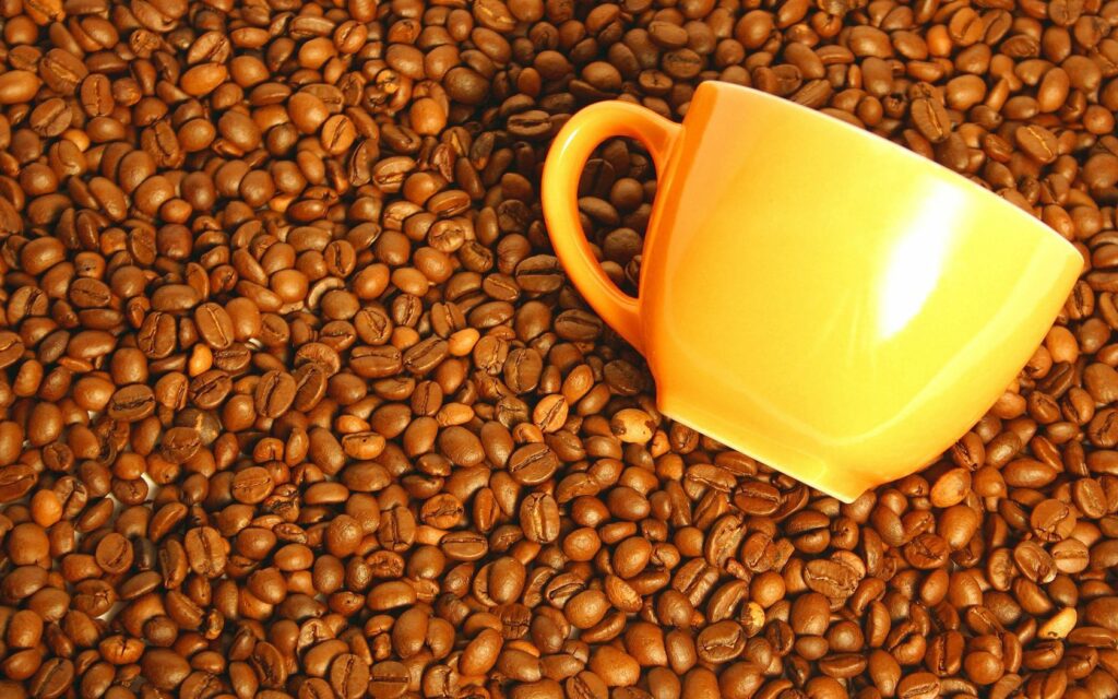 Vibrant Yellow Coffee Cup on Rich Coffee Beans - Inviting Wallpaper