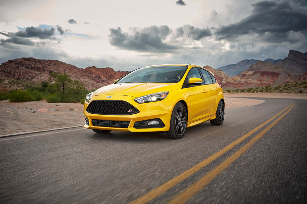 Vibrant yellow Ford Focus ST on open road with dramatic cloudy sky sporty car wallpaper background