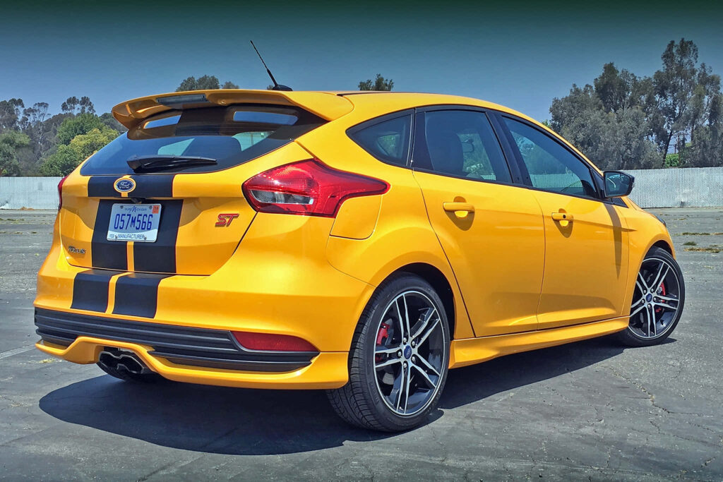 Yellow Ford Focus ST with black racing stripes and spoiler parked on sunny pavement background Wallpaper