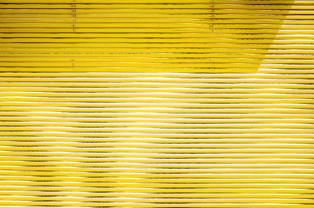 Vibrant yellow rolling shutter with geometric horizontal metal lines wallpaper background
