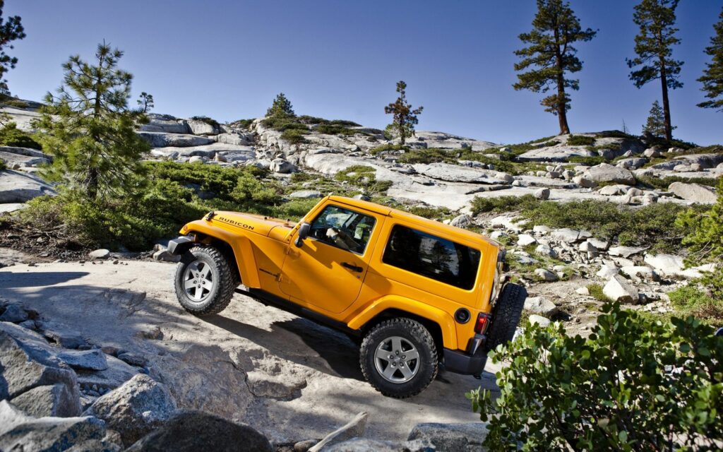 Vibrant Yellow Jeep Wrangler on Rugged Terrain - Adventure Background Wallpaper