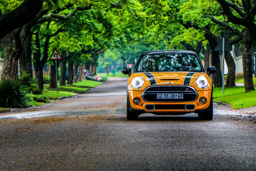 Vibrant Yellow Mini Cooper S on Scenic Tree-Lined Street Wallpaper