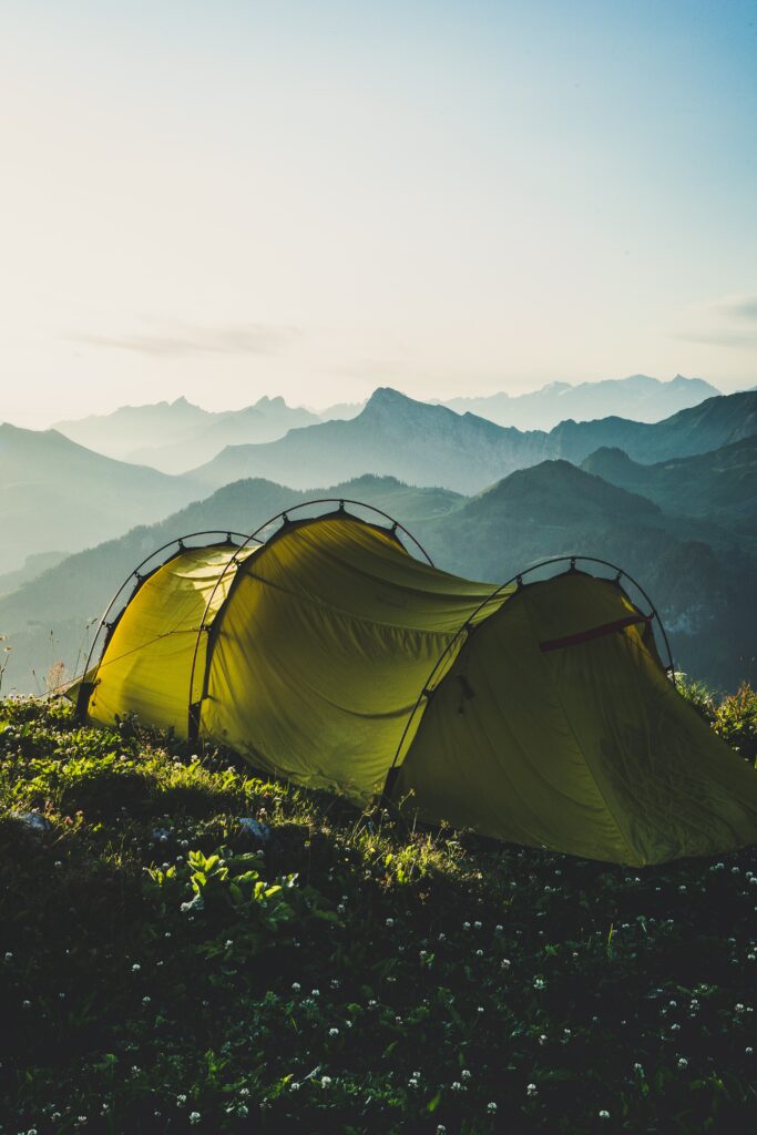 Yellow camping tent on grassy mountain ridge with misty blue mountains at sunrise outdoors Wallpaper