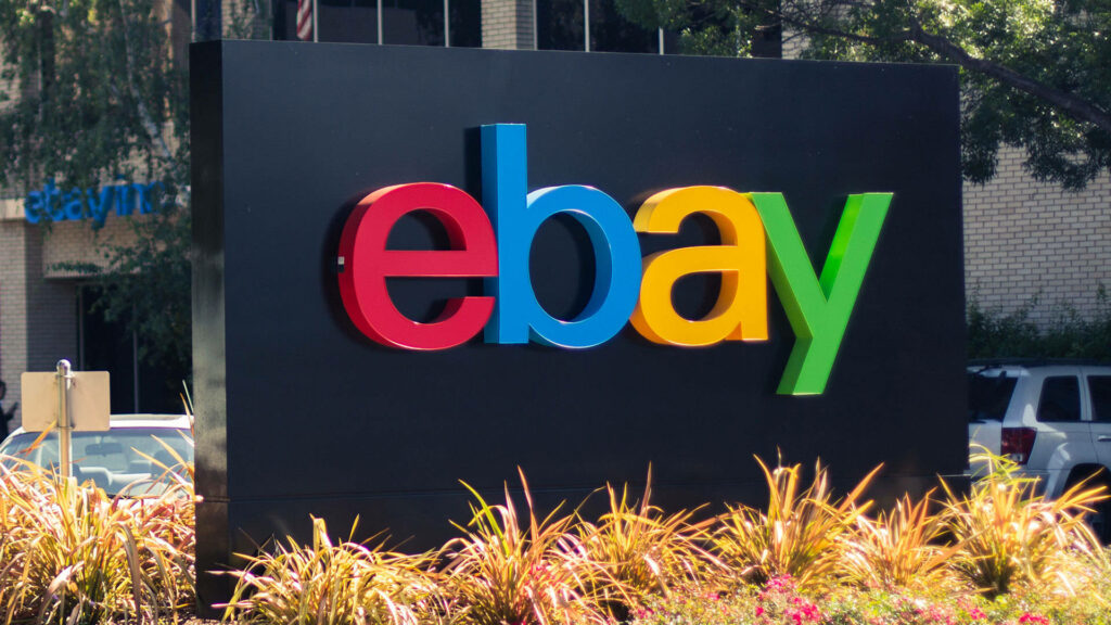 eBay logo in vibrant colors on black sign with greenery and modern architecture background Wallpaper