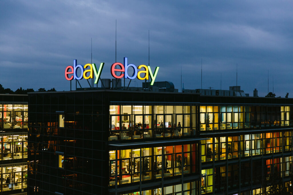 eBay logo glowing on glass office building at dusk with illuminated windows and deep blue sky Wallpaper