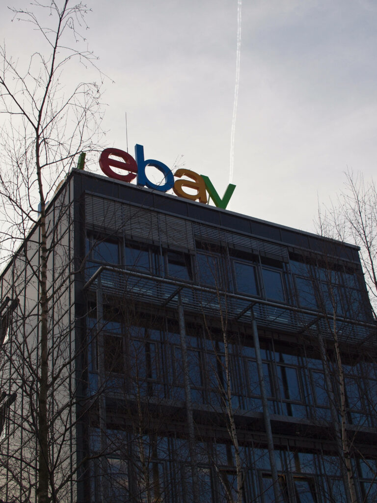 eBay logo in vibrant colors on modern glass building with bare tree branches and clear sky Wallpaper