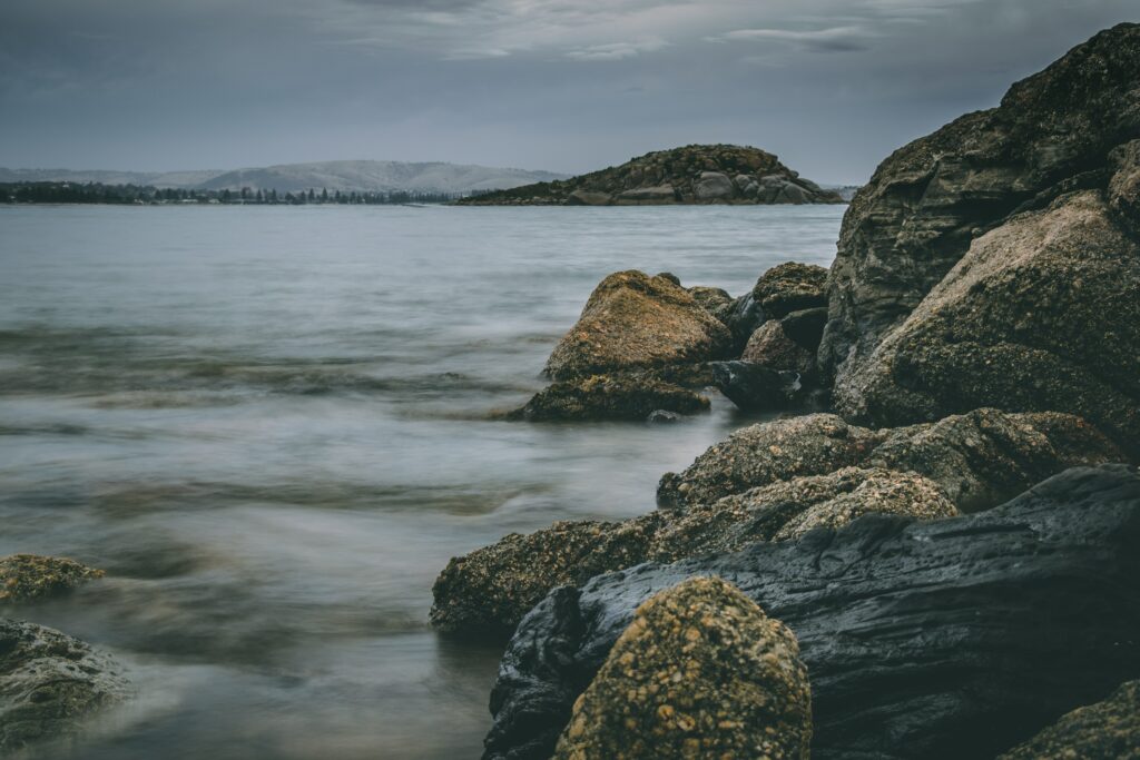Victor Harbor shore with rugged stones gentle waves and moody overcast sky coastal wallpaper background
