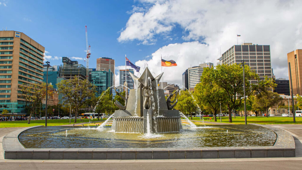 Victoria Square fountain in Adelaide with city skyline green trees and flags under blue sky wallpaper