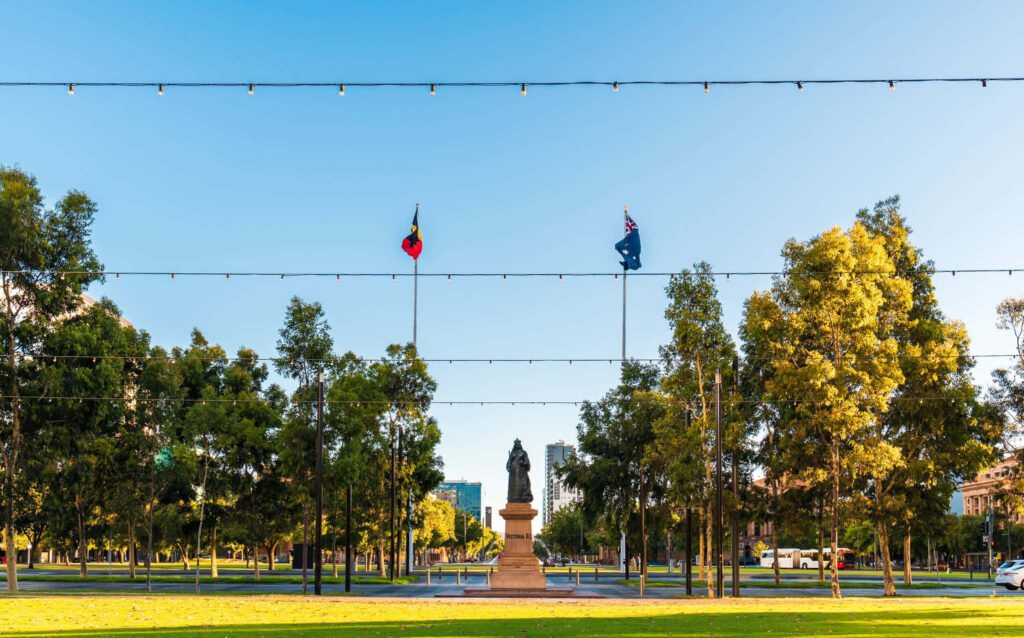 Iconic Victoria Square statue Adelaide with Aboriginal Australian flags and green trees background Wallpaper