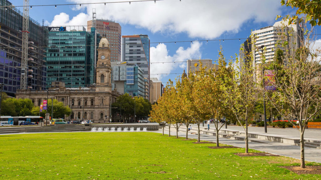 Victoria Square Adelaide vibrant urban park with green lawns historic and modern buildings background Wallpaper