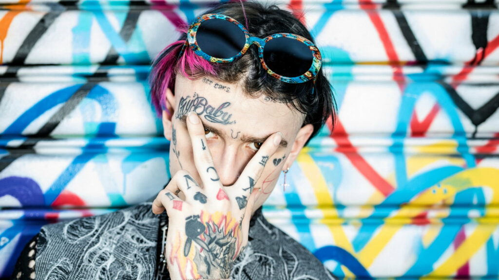 Lil Peep HD wallpaper showing CryBaby face tattoos pink hair victory sign urban graffiti background